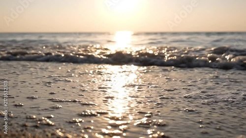 Ocean waves washing onto a sandy beach at sunset with sunlight reflecting on the water surface with sunlight shimmering wet during golden sunset angle view gentle video low angle