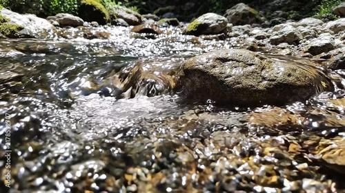 Clear water flowing over smooth stones in a sunlit stream with sparkling reflections with video clear environment shimmering glistening wilderness background freshwater