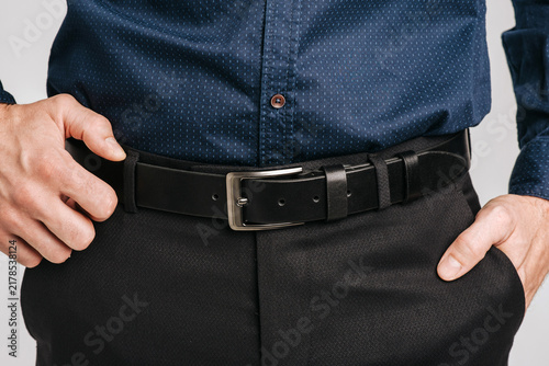 Close-up of a man wearing a black smooth leather belt with a classic metal buckle on black trousers