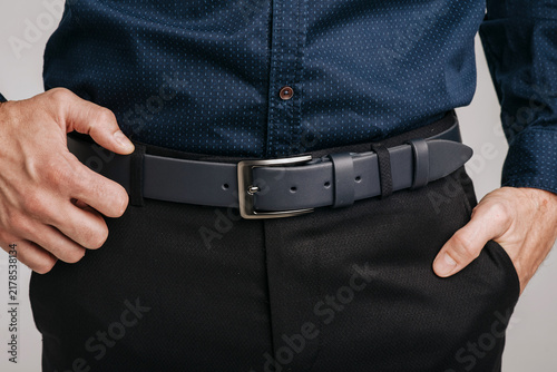 Close-up of a man wearing a dark blue smooth leather belt with a classic metal buckle on black trousers