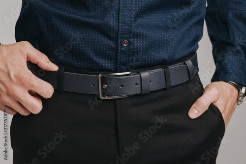 Close-up of a man wearing a dark blue stitched leather belt with a classic metal buckle on black trousers