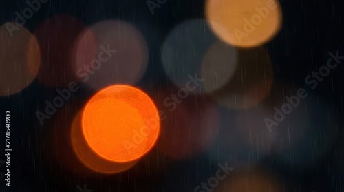 Soft orange and yellow bokeh lights glow through falling rain in a dark atmospheric night scene