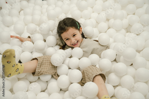 Young girl laughs joyfully while playing in a ball pit filled with soft white balls
