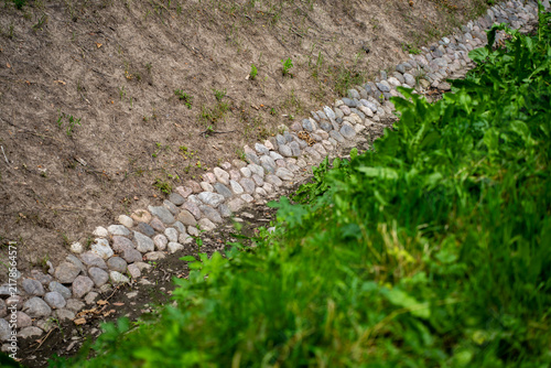 фотографія Stone lined drainage ditch and rainwater runoff canal built with cobblestones on earth embankment near green grass