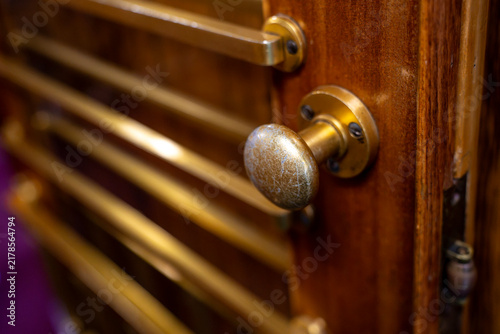 Fotografie Close up of vintage brass doorknob installed on polished wooden door with horizontal ventilation louver slatted panels