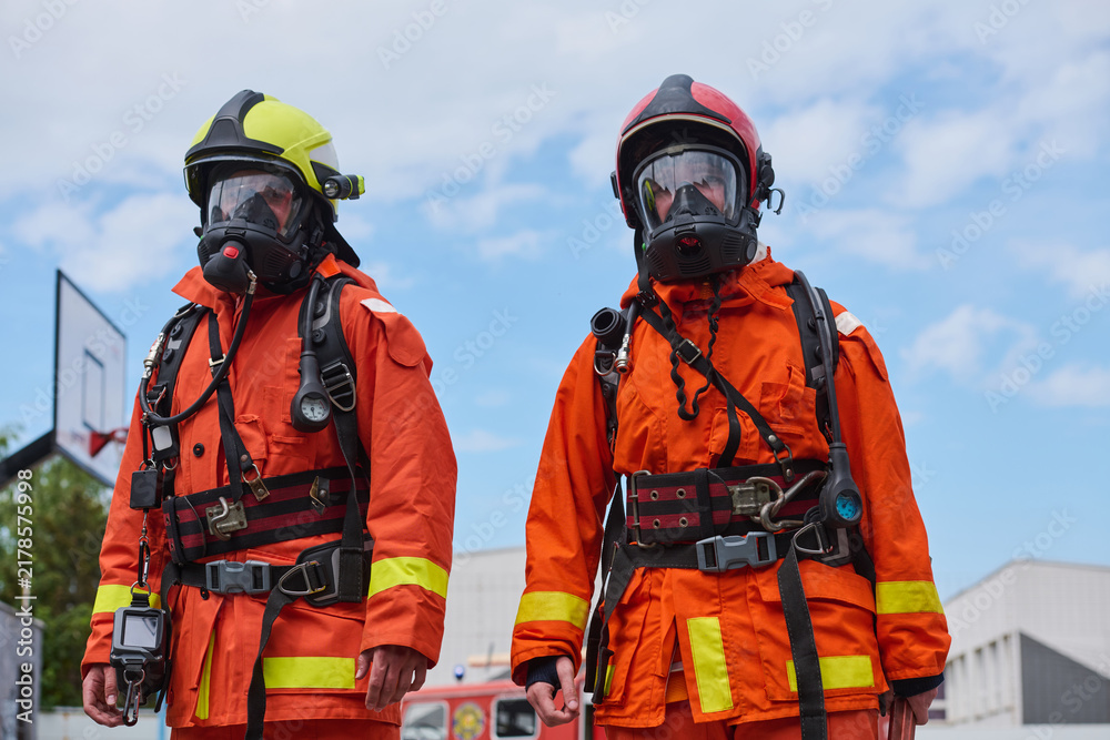 Fototapeta premium Two Firefighters in Orange Protective Gear Wearing Breathing Apparatus and Helmets During Training Drill