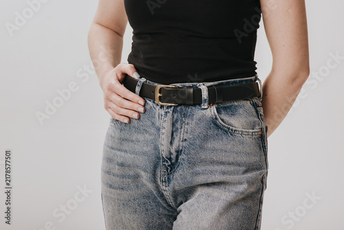 Close-up of a woman wearing a black smooth leather belt with a gold metal buckle on acid wash jeans