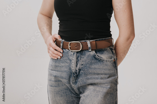 Close-up of a woman wearing a brown smooth leather belt with a rounded silver buckle on acid wash jeans