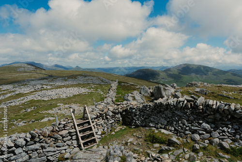 View of the rugged Nantlle Ridge landscape featuring a traditional dry stone wall with a wooden stile, set against rolling hills in Nantlle, Wales, United Kingdom.