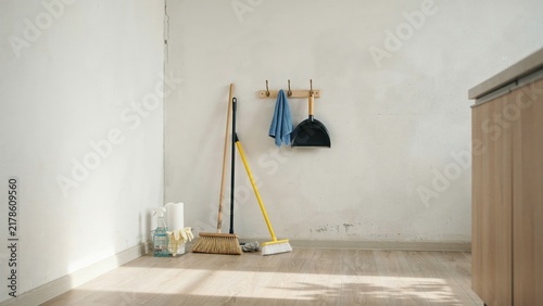 Cleaning tools with yellow and black brooms plus white paper towel organized in corner against white wall for housekeeping.