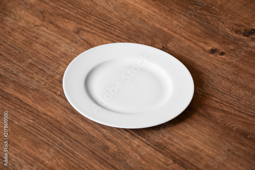 Ceramic white flat plate for food on wooden table top view