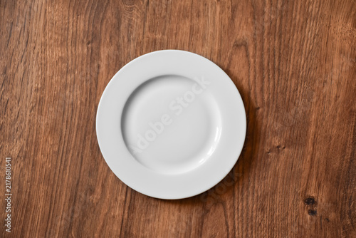 Ceramic white flat plate for food on wooden table top view