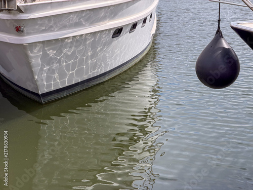 Black Rubber Boat Fender Hanging Beside Moored White Yacht Hull at Marina Dock