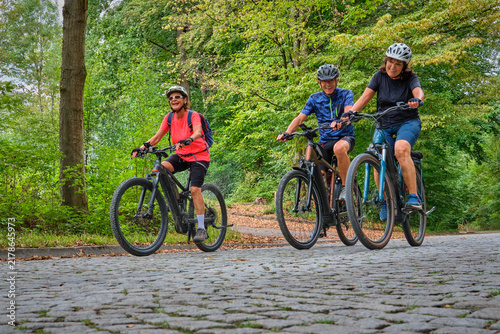 Three senior friends enjoy a cycling tour through a peaceful forest on a sunny day, promoting friendship, fitness and active aging in Naturpark Schönbuch, Herrenberg, Baden-Württemberg, Germany.