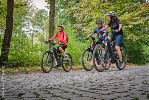 Three senior friends enjoy a cycling tour through a peaceful forest on a sunny day, promoting friendship, fitness and active aging in Naturpark Schönbuch, Herrenberg, Baden-Württemberg, Germany.