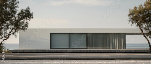 Minimalist long single story white modern villa sitting on wooden deck on sandy beach framed by two windswept coastal trees overlooking calm blue ocean