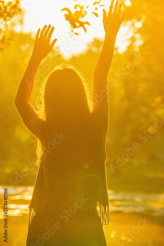 Teenage girl raising her hands toward the morning sun in a joyful greeting.