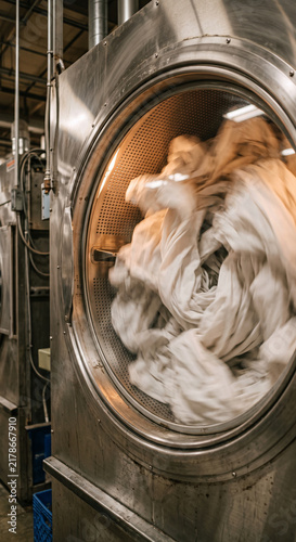 Canvastavla White sheets tumbling inside the illuminated drum of a large stainless industrial washing machine, with circular metal opening, motion blur, perforated drum