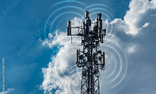 Cell tower with multiple antennas broadcasting signal waves. Dramatic blue sky with clouds. Ideal for telecom, wireless network, and mobile technology editorial or marketing content.