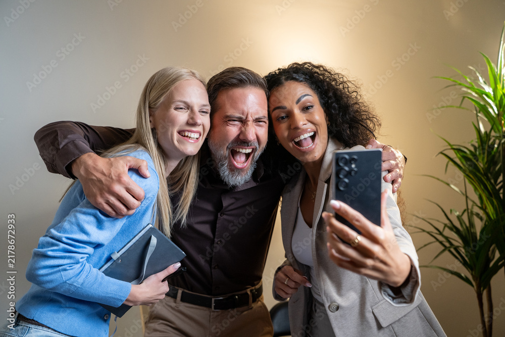 Obraz premium Diverse businesspeople smiling and taking a selfie together in a modern office, showing on social media teamwork and camaraderie between work. 
