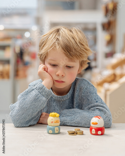 Young boy thoughtfully observes colorful piggy banks on a table in a bright store setting