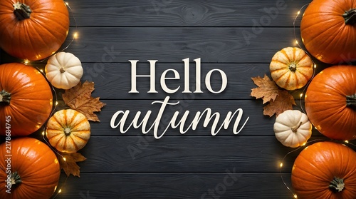 Hello autumn text sign surrounded by orange and white pumpkins on a dark wooden background