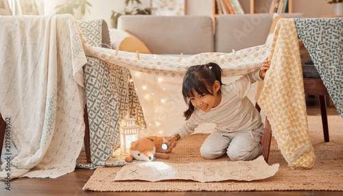 Child playing under a makeshift blanket fort with fairy lights and a stuffed animal.