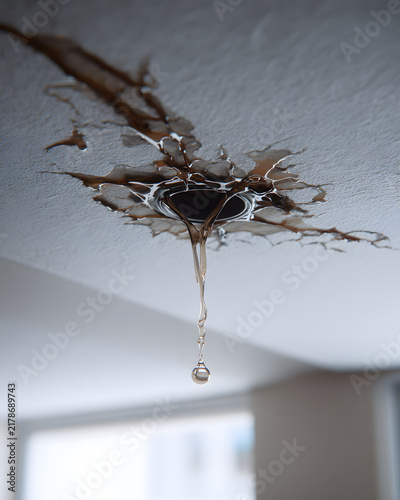 Close-up of a leaking ceiling with a water droplet dripping from a damaged area, indicating home repair or water damage issues.