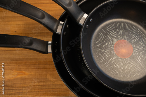 Obraz na plátne Black non-stick frying pans with handles on a wooden table, preparing healthy fo