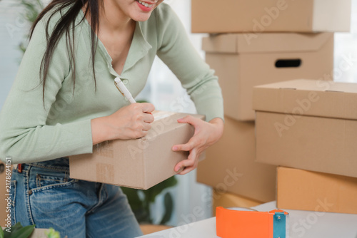 Картината върху платно Shipping Preparation: A young woman diligently writing on a package, surrounded by stacks of cardboard boxes, prepares for shipment in a well-organized workspace, ready to fulfill orders