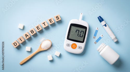 Flat lay of diabetes tools including a glucometer, sugar cubes, lancet pen, and letter blocks on blue