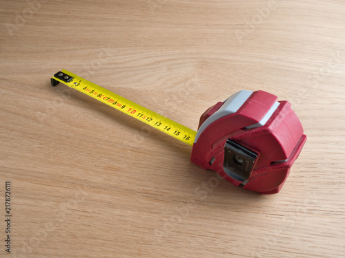 Canvastavla Red Tape Measure Extended on Wood - A red and grey retractable tape measure fully extended on a light wooden surface, showing metric markings