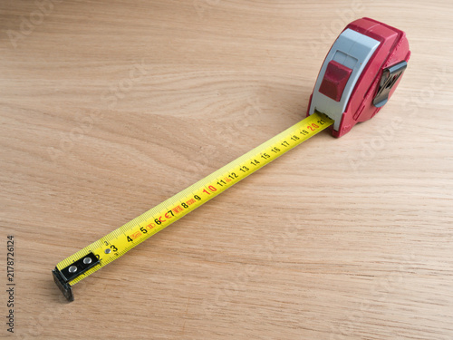 Canvastavla Red Tape Measure Extended on Wood - A red and grey retractable tape measure fully extended on a light wooden surface, showing metric markings