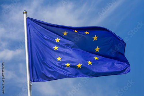 Flag of the European Union waving in the wind on flagpole against the sky with clouds on sunny day, close-up