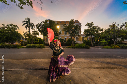 A sturdy Latina-Gypsy woman dancing traditional dances in the streets of Mérida, Yucatán, Mexico; the famous Regional Museum of Anthropology (Palacio Cantón) is visible in the background.
