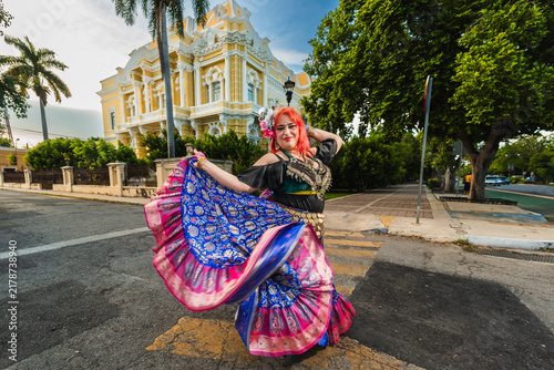 A sturdy Latina-Gypsy woman dancing traditional dances in the streets of Mérida, Yucatán, Mexico; the famous Regional Museum of Anthropology (Palacio Cantón) is visible in the background.
