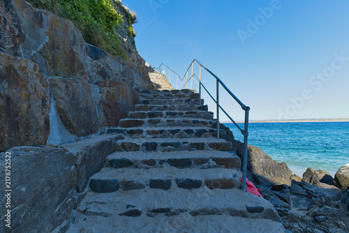 Photography Stone steps climb a rocky cliff beside a bright blue ocean under a clear sky