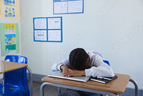 Closed silver laptop and black notebook are resting on wooden school desk in classroom