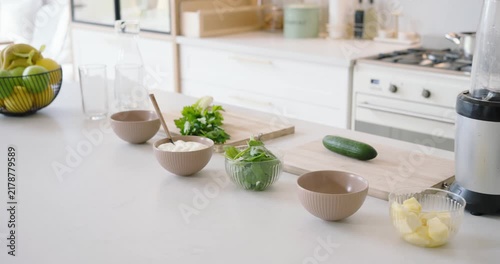 Camera is slowly panning left from right to show blender, cucumber, herbs, bowls, butter on counter