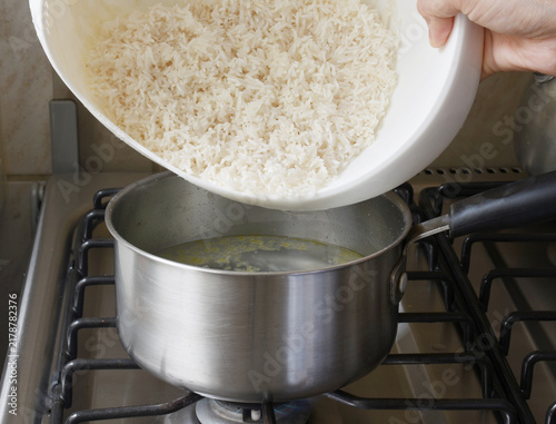 Fotografía Close-up of a hand adding uncooked white rice to a pot of water, showing a simple step in rice preparation and homemade cooking