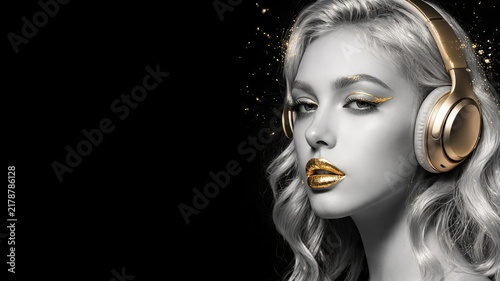Blonde girl gold headphones  black white face gold lips makeup  wavy light hair. Golden sparkle dust black background  luxury beauty art portrait. Girl gold headphones shine