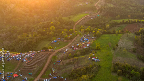 Aerial view of the Rally 2026 Paraguay event with spectators, vehicles, and tents along winding dirt roads in a hilly landscape during golden hour in Nueva Alborada, Itapua Department, Paraguay.