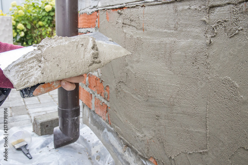 Worker spreads gray mortar on unfinished brick wall