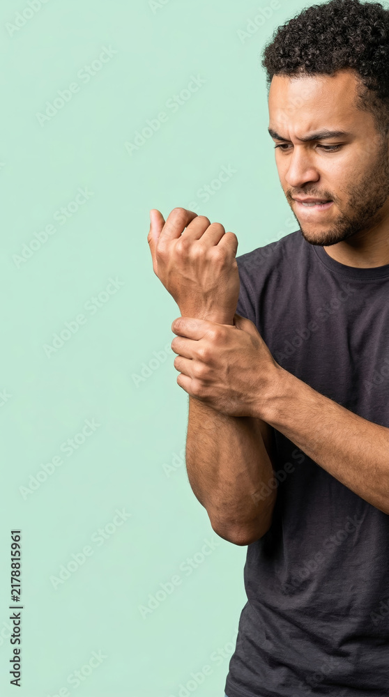 Naklejka premium Man suffering from wrist pain holding his arm. Young male in agony after injury to hand. Chronic discomfort, medical problem, health issue. Isolated on green background with copy space.