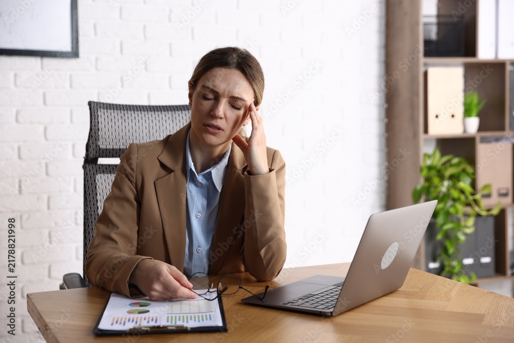 Fototapeta premium Stressed businesswoman in suit with glasses near laptop at desk in office