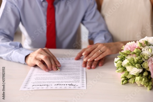 Couple signing marriage contract at light wooden table, closeup