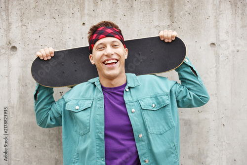Foto Happy man with skateboard near grey wall outdoors