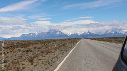 Slow-motion clip showing the rear of a passenger car traveling along a highway in Argentine Patagonia, leaving behind a snow-capped mountain range in Los Glaciares National Park.