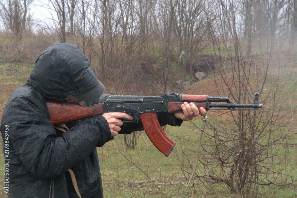 Fototapeta premium Person in black waterproof jacket and hood aiming rifle outdoors