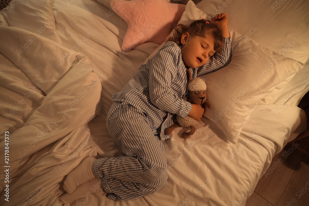 Fototapeta premium Adorable little girl with plush sheep sleeping in bed